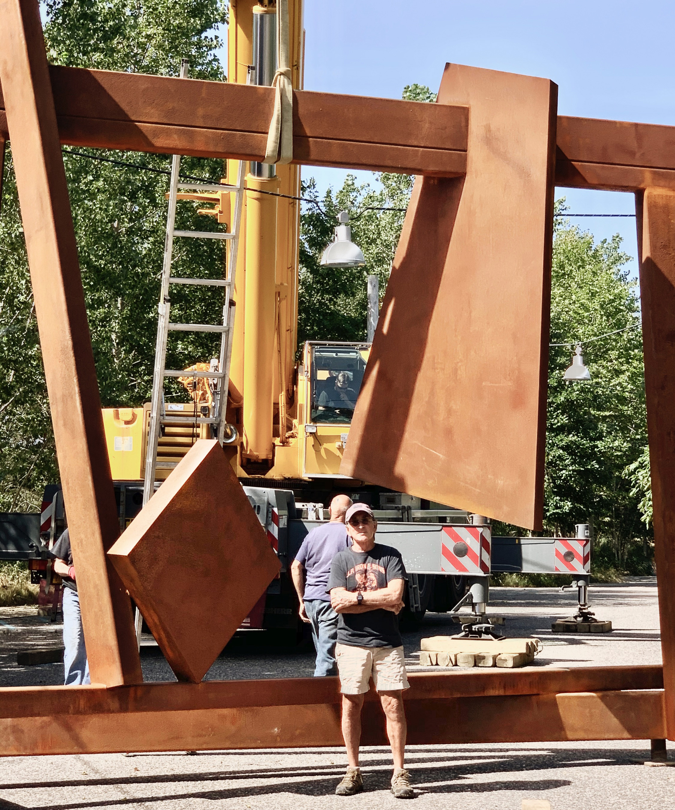 Man standing in front of a large metal sculpture being installed with machinery