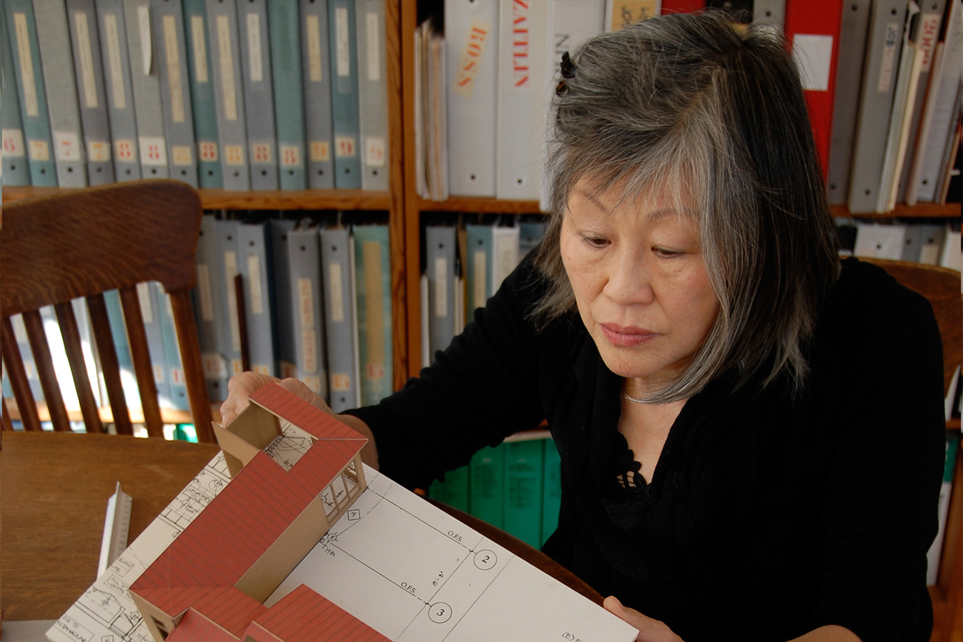Photo of an older Asian woman reviewing a small architectural model