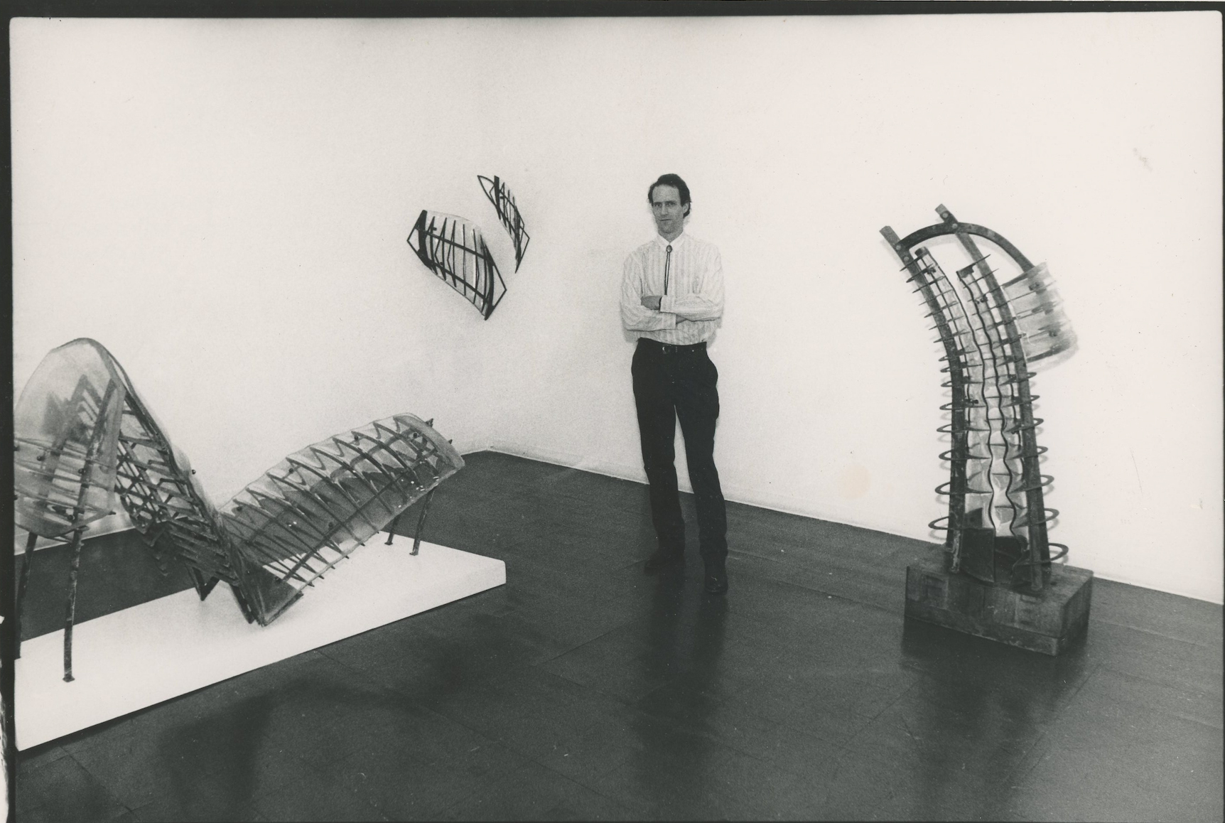 A black-and-white photo of a man standing between sculptures.