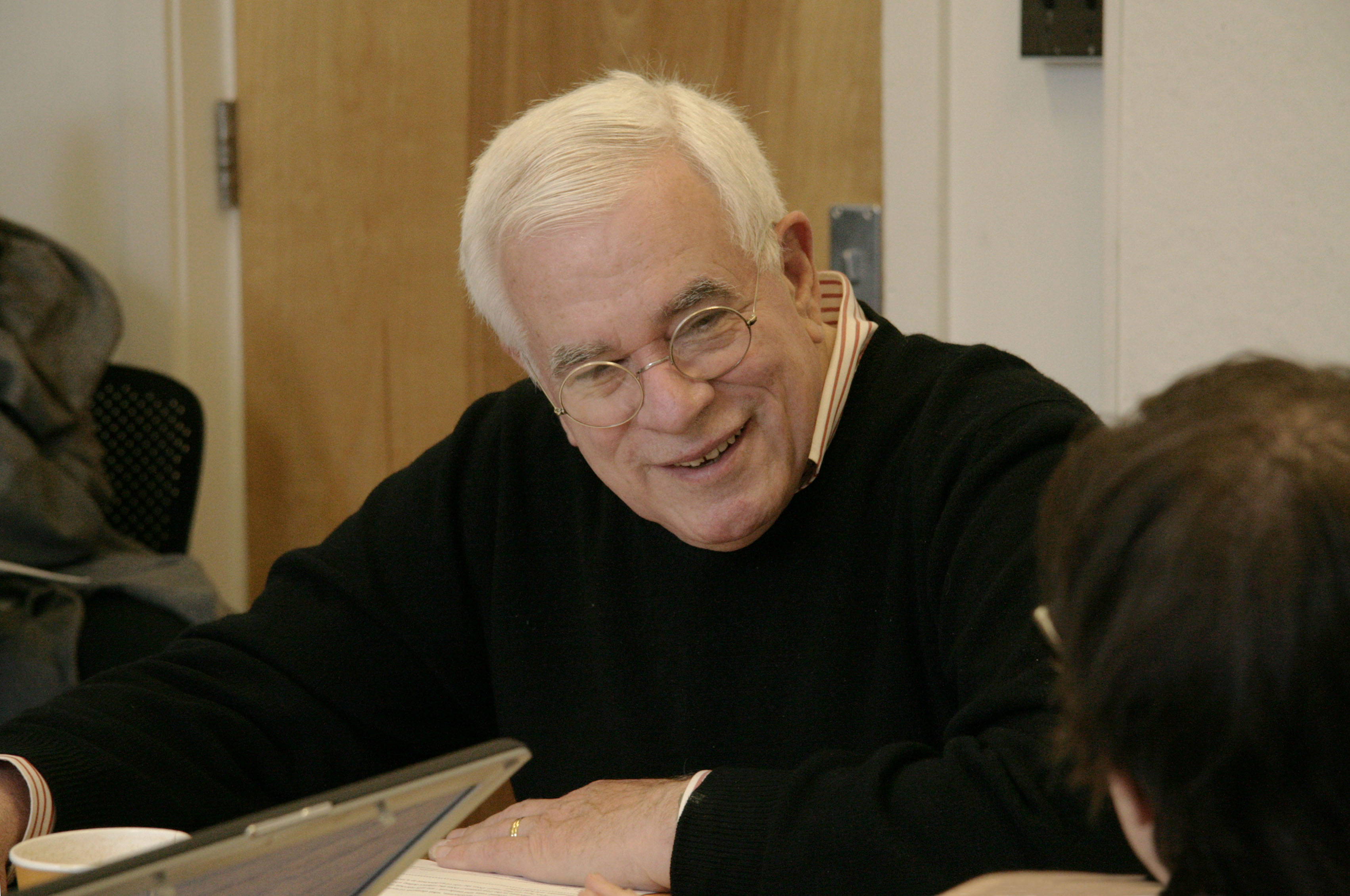 An older man sits at a table, engaging in conversation.