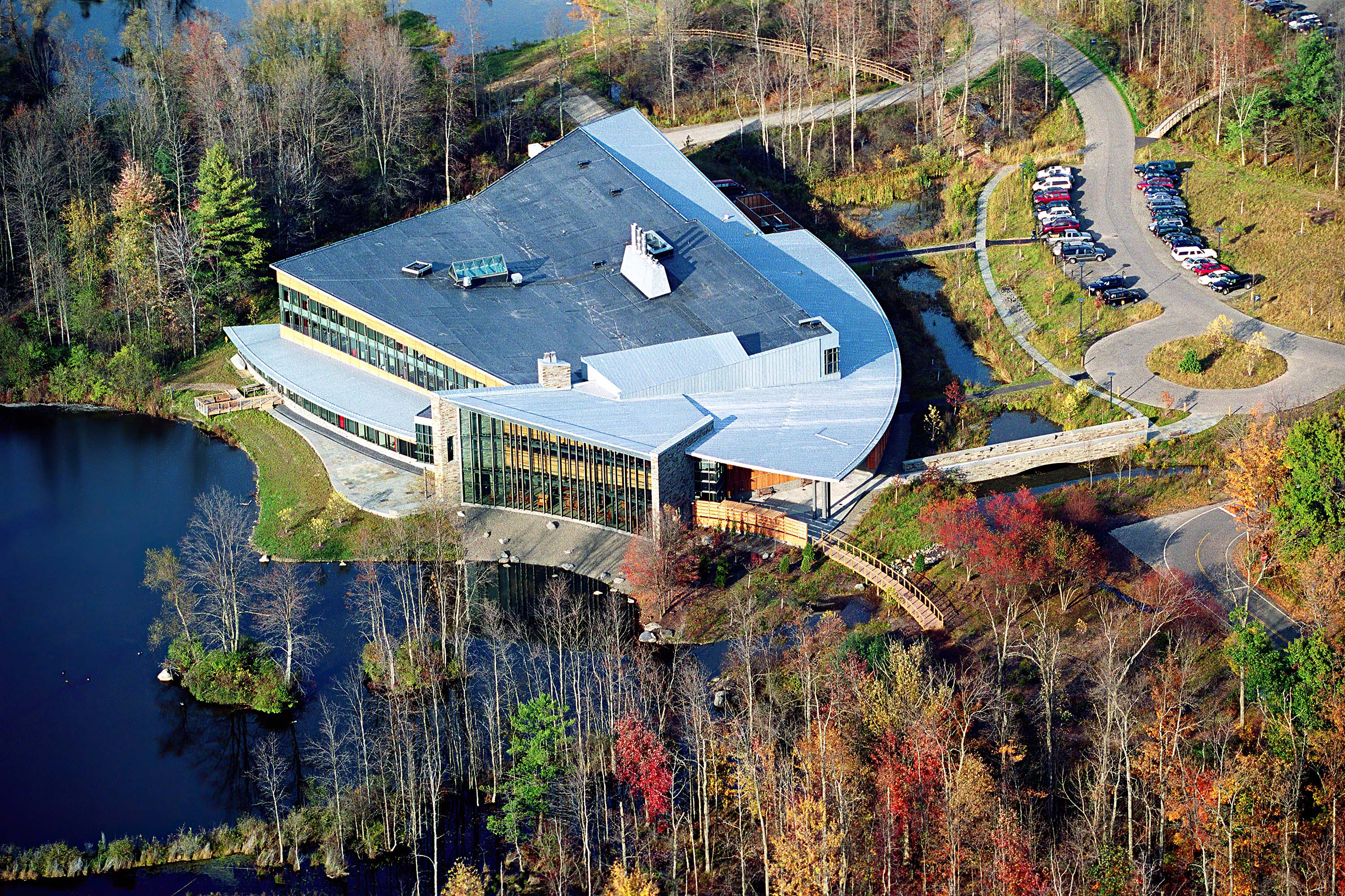 Aerial view of a building overlooking a large pond, surrounded by wooded areas.