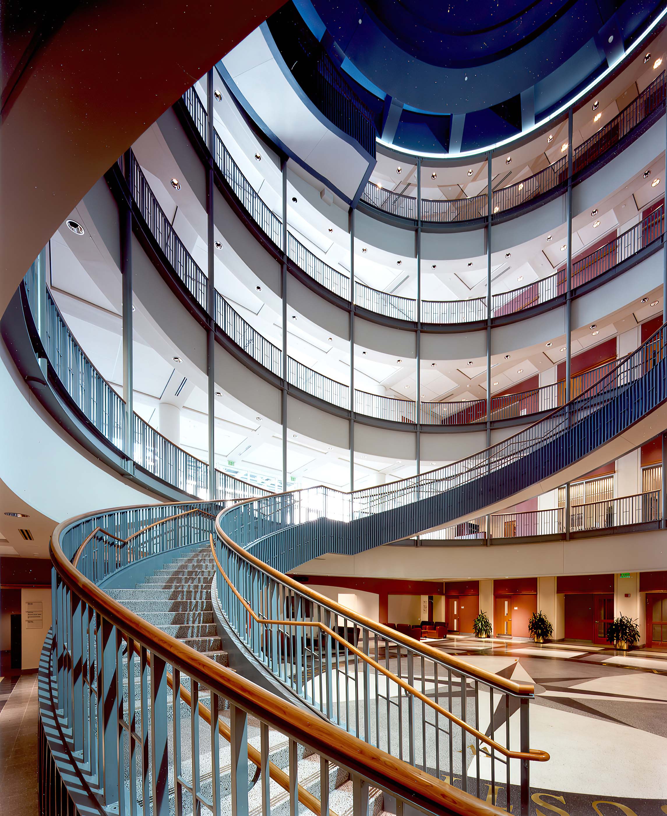 A 5-story circular room with balconies overlooking the first floor atrium where a curving staircase begins.