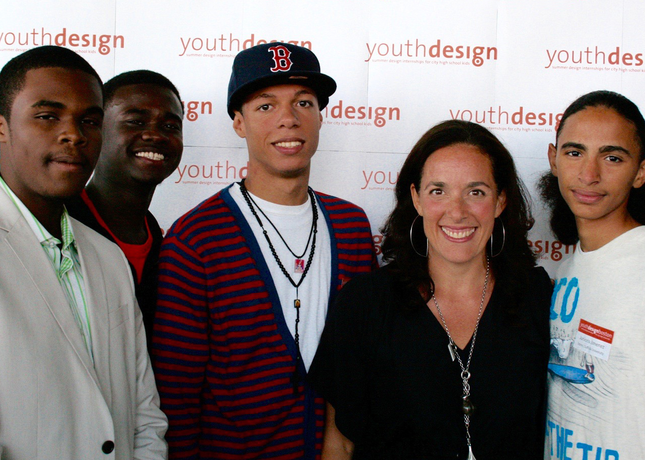 Four male teenagers pose with an adult woman in front of a white backdrop with the words youth design printed in red text