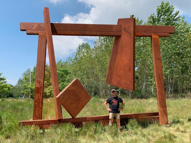 man with large metal sculpture in an open field