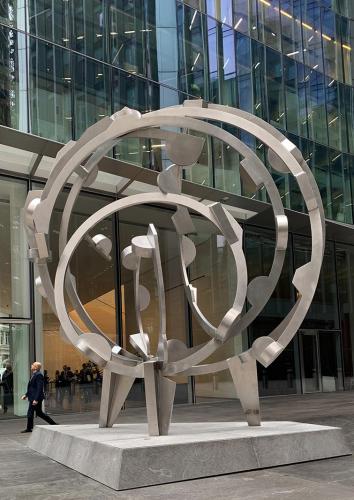 large sculpture of silver concentric circles in front of a glass building