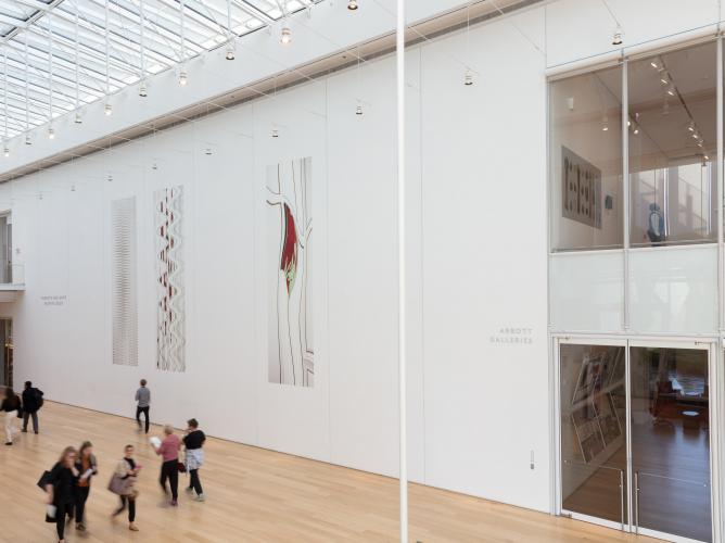 image of art on the wall in an open atrium with skylights and people on walking on the wood floor