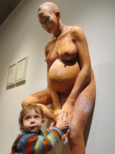 sculpture of a pregnant woman against the wall and a young boy touching the sculpture