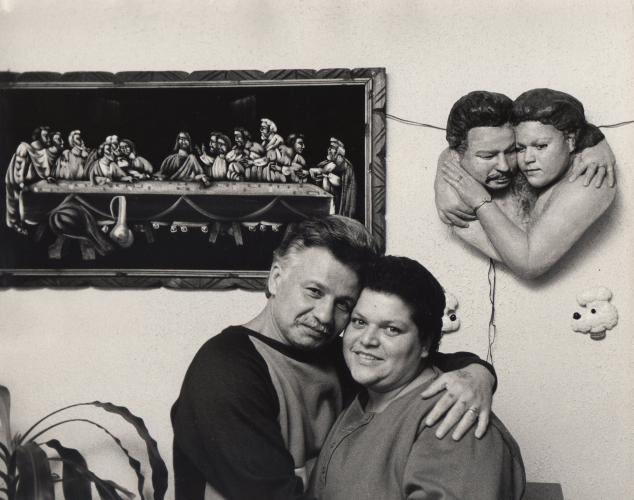 a black and white photo of a man and woman hugging in front of a wall relief sculpture of them embracing