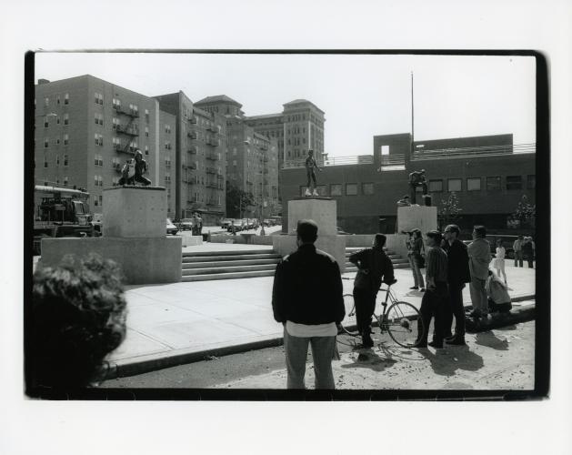 black and white photo of people looking at sculptures outdoor in an urban area