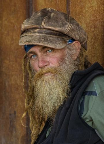 An older man with a mostly white bead looks into the camera