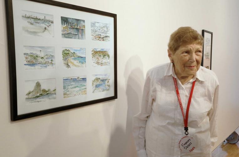 Frances Shloss poses with her framed watercolor paintings hanging on a wall