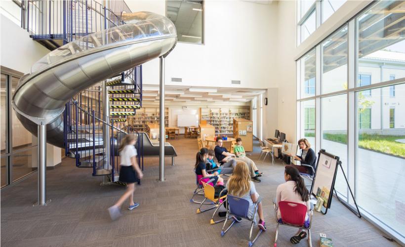 Adolescents and teacher meeting in room with winding staircase and enclosed slide