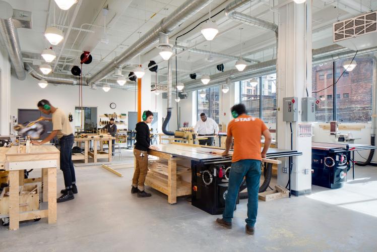 People working with wood and power tools in a workshop.