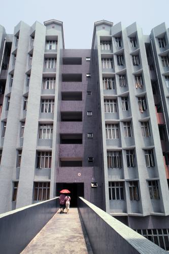 Skywalk leading to an entryway of a gray multistory apartment building.