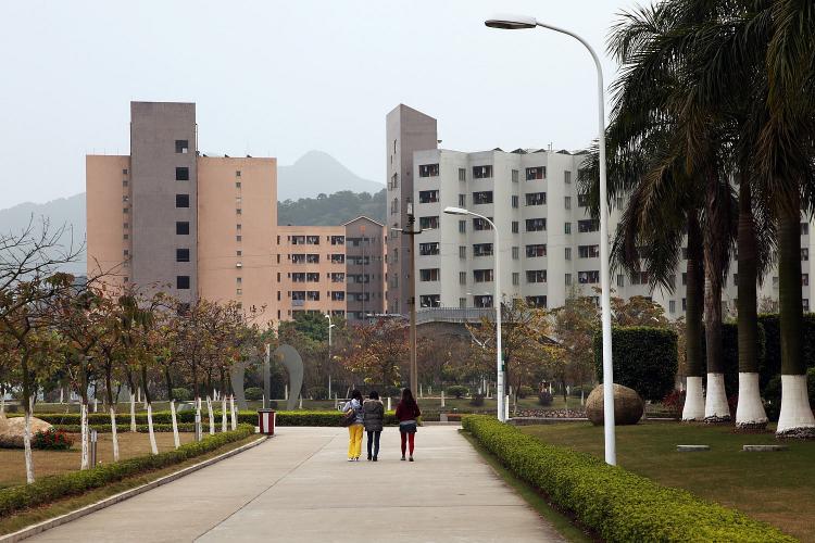 Three people walk down a wide sidewalk toward dormitories. 