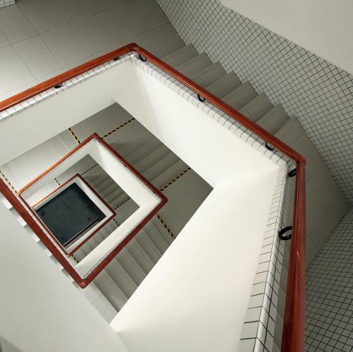 View of a rectangular stairwell with white walls and stairs and wooden railings. 