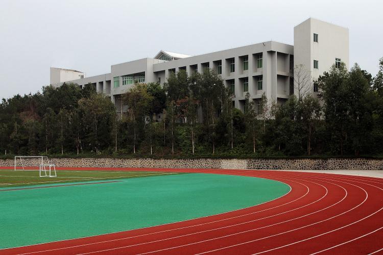 A rectangular building sits behind a running track and sports field.