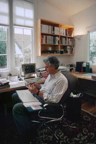 An older man sits next to a desk with a small, older computer model.