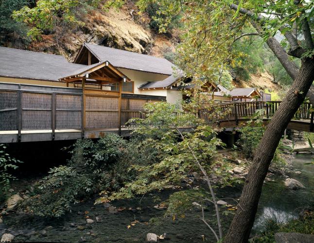 A wooden bridge crosses a creek, providing a path to the bath house.