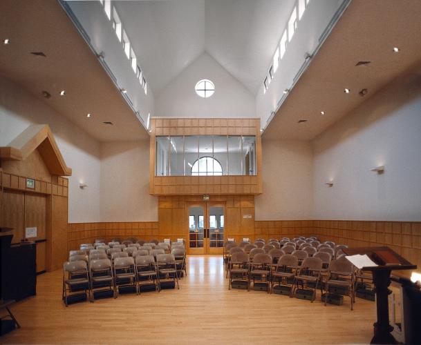 A small chapel with white walls, wooden doorways and trim, and metal folding chairs. 