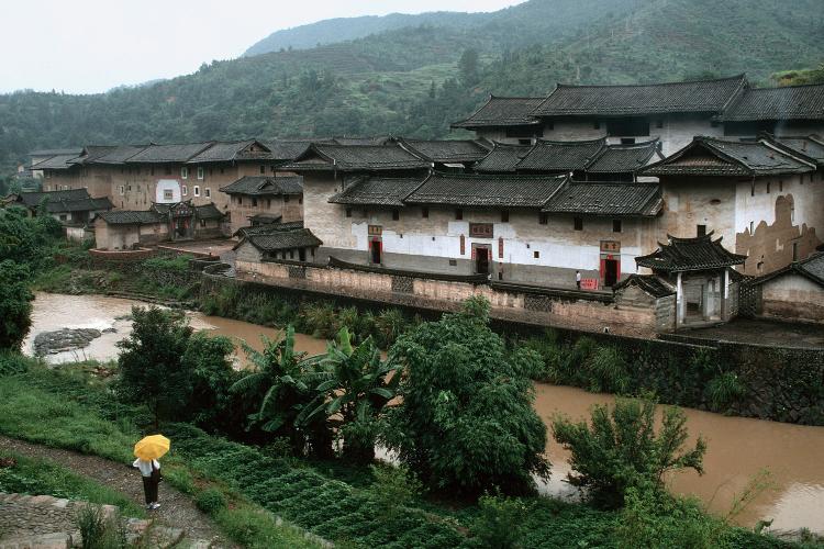 Exterior view of weathered square clan houses overlooking a narrow stream of water.