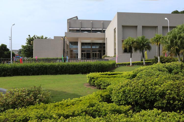 Exterior view of a beige building and lush greenery.
