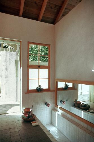 A long mirror lines the wall next to a tiled tub. An open doorway and a window overlook the tub. 