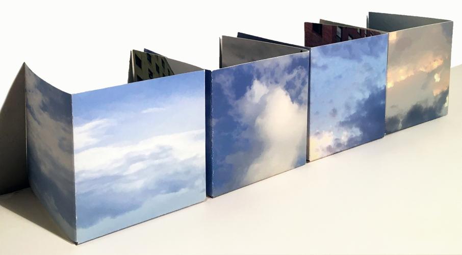 Back views of a digitally printed unique artist’s book housed in a found box. Three of the 3D pages depict blue skies and white clouds, the last page depicts a dreary, gray sky.