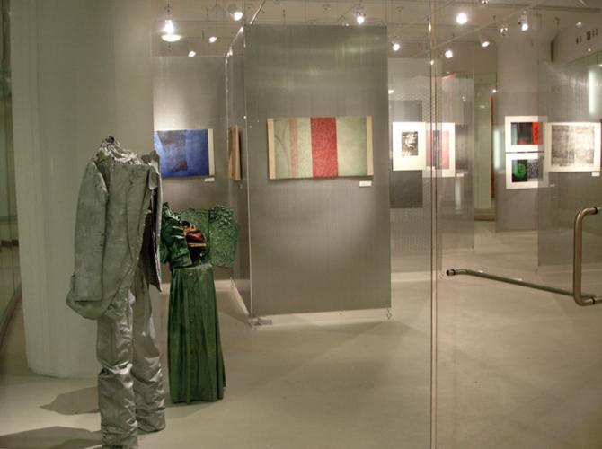 A art exhibition showcases two distressed outfits displayed three-dimensionally and art prints hanging on walls. 