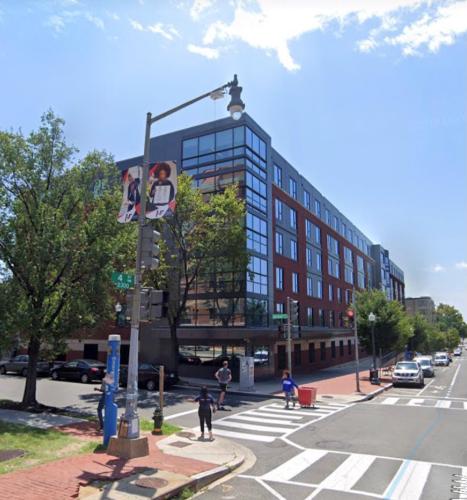 People cross the street in front of a large building on a bright, sunny day.