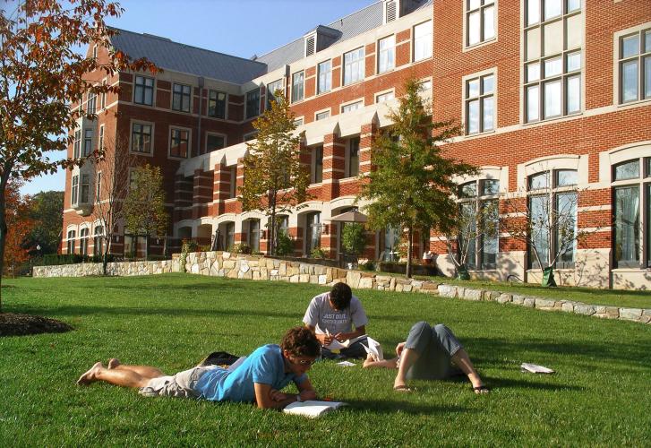 Students lie on the grass outside a brick building.