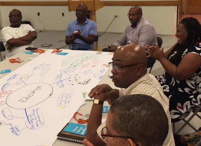 A group of adult Black men and one Black woman sit around a table where they created a diagram on a large sheet of paper.