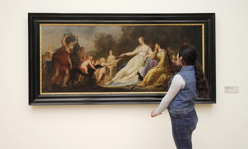 A teenage girl looks at a painting of a woman who is surrounded by adults and being approached by two cherubic children. 