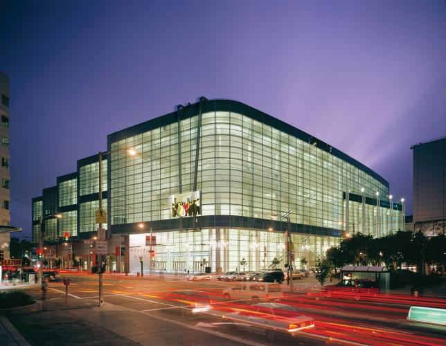 A well-lit, multifloor glass building stands out against a purple night sky. The building's interior lights highlight the curved edges of the main building's facade.