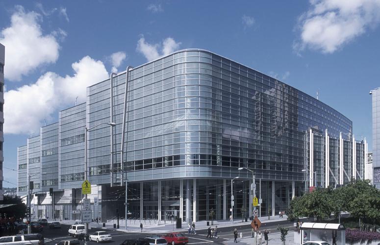 The glass facade of a multistory building reflects surrounding clouds on a blue-sky day.