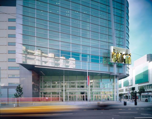 Street view of a building's glass-walled entrance and upper floors.
