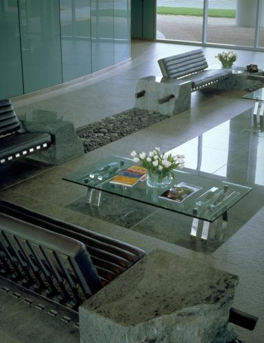 Interior view of a lobby designed with matte stone surfaces accented by a glass table on an inlay of shiny tile. 