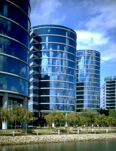 Three tall, pillar-shaped buildings reflect the surrounding clouds and bright blue sky.