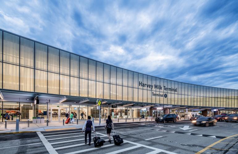 Exterior view of an airport terminal. A long curving facade is lit with a yellow glow from the interior lights.