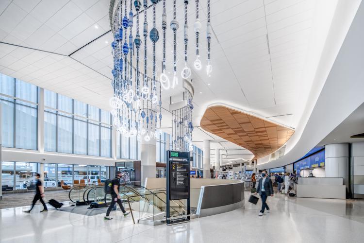 A fringe-like art sculpture hangs over an escalator in an airport terminal.
