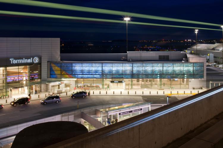 Exterior view of an airport terminal at night. A blue glow lights up a wing extending from the main terminal entrance.