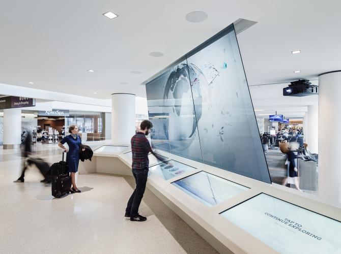 A man uses a touchscreen interface in front of a large flat-screen display. 