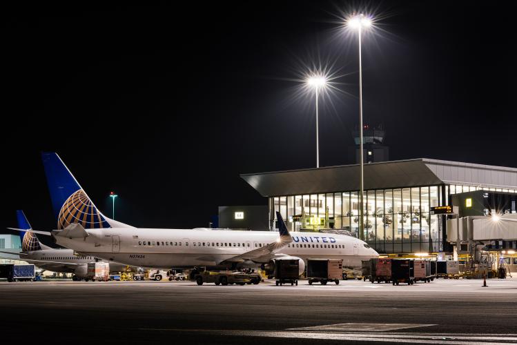 A passenger airplane is parked outside of an airport terminal at night.