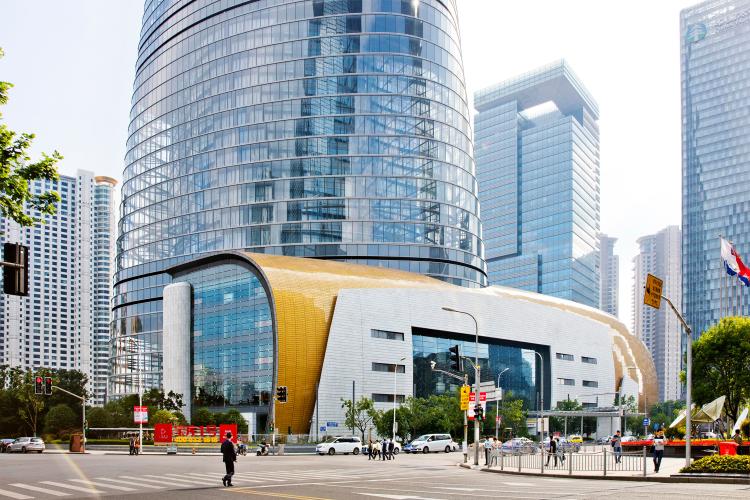 A multistory, copper-clad building faces the street at the base of a transparent skyscraper.