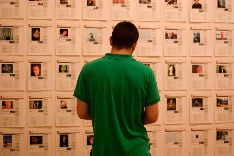 View of the back of a man dressed in a green shirt as he looks at papers covering a wall.