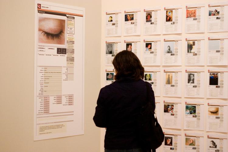 A woman looks at dating profiles printed and displayed on two walls.