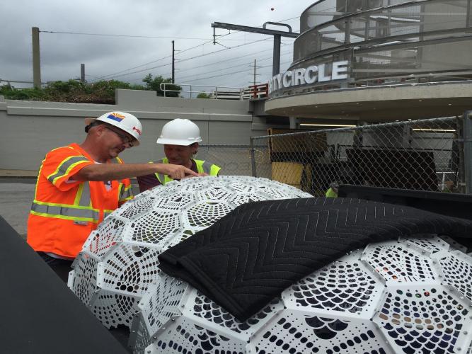 Two construction workers look over two large white doily sculptures.
