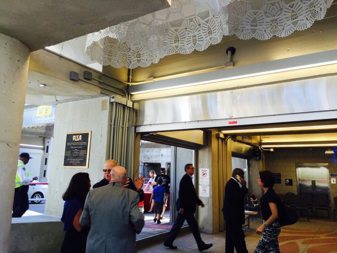 Large white doily sculptures hang from the ceiling as people move through an industrial-looking space