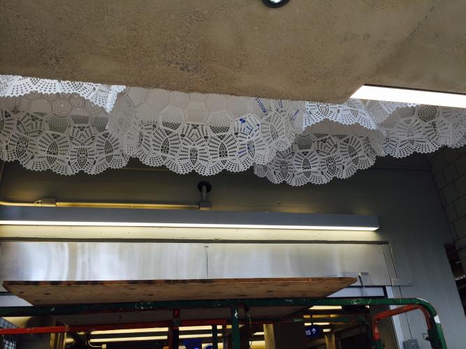 Large white doily sculptures hang from the ceiling between lower concrete and metal entryways.