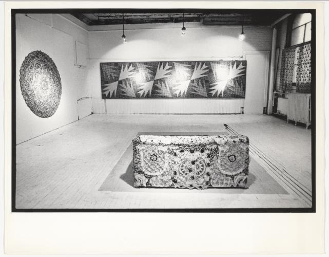 Black-and-white photo of an installation featuring a patterned couch and patterned wall decor.